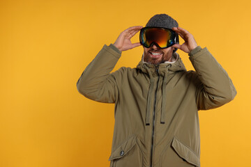 Winter sports. Happy man in ski suit and goggles on orange background, space for text