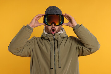Winter sports. Emotional man in ski suit and goggles on orange background