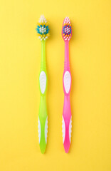 Colorful plastic toothbrushes on yellow background, flat lay