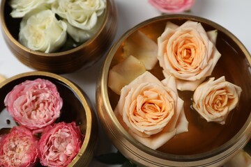 Obraz na płótnie Canvas Tibetan singing bowls with water and different beautiful rose flowers on white background, above view