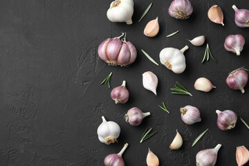 Fresh garlic and rosemary on dark textured table, flat lay. Space for text