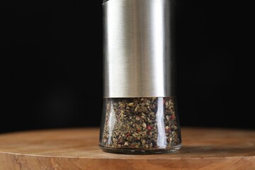 Pepper shaker on wooden board against black background, closeup