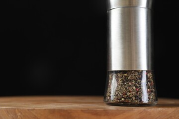Pepper shaker on wooden board against black background, closeup. Space for text