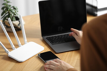 Woman with smartphone and laptop connecting to internet via Wi-Fi router at table indoors, closeup