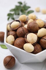 Tasty Macadamia nuts in bowl on white table, closeup
