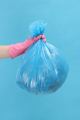 Woman holding plastic bag full of garbage on light blue background, closeup