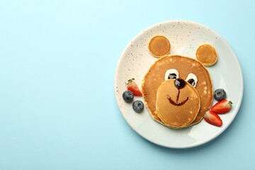 Creative serving for kids. Plate with cute bear made of pancakes and berries on light blue table, top view. Space for text - obrazy, fototapety, plakaty