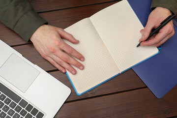 Man taking notes at wooden table, top view