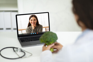 Fototapeta na wymiar Doctor dietician have online consultation with woman patient, holding broccoli