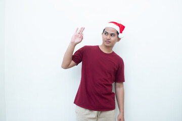 Young Asian man wearing a Santa Claus hat with a hand making the ok gesture isolated by a white background for visual communication