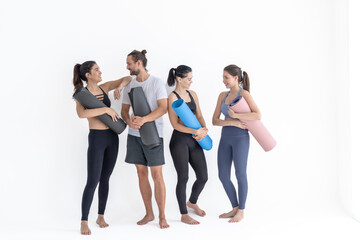 Obraz premium Group of happy sporty girls and guy wearing body stylish sportswear holding personal carpets leaned on a white background. waiting for yoga class or body weight class. healthy lifestyle and wellness
