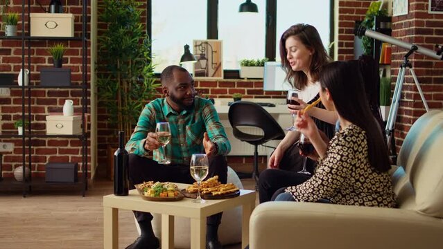 Friends laughing, drinking red and white wine, talking about their lives in cozy apartment living room. Colleagues spending time with each other, eating from charcuterie board at home, zoom in shot