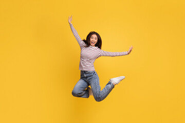 Overjoyed young chinese lady 20s jumping on yellow background