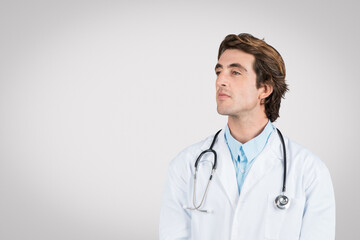 Fototapeta premium Thoughtful caucasian male doctor in white coat with stethoscope