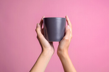 Two beautiful female hands holding black mug in palms for mockup isolated on pink background.