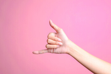 Woman hand showing calling hand gesture or shaka sign on pink background
