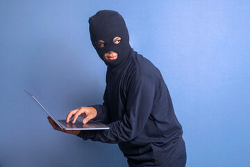 Man hacker in black mask using computer laptop to stealing data. 