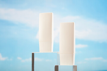 Blank label tube in white color placed on glass podiums over the blue sky background. Mockup for...