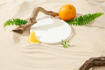 Fototapeta na wymiar Close-up of a round white platform placed on a white sand background with dry branches, fern leaves and fresh oranges. Tropical atmosphere with copy space.