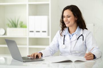 Young woman doctor using laptop at clinic, telemedicine concept - obrazy, fototapety, plakaty