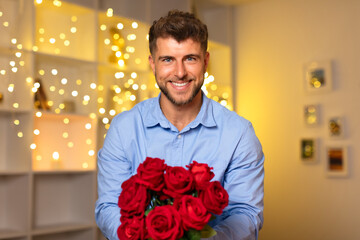 Smiling man with bouquet of red roses, festive background lights
