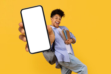 Happy black guy student showing smartphone screen on yellow backdrop