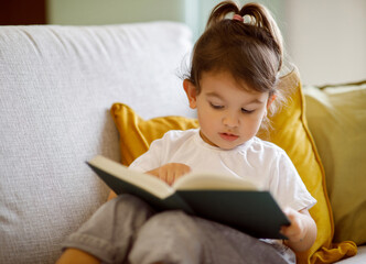 Small child relaxing on couch with book, experiencing the joy of reading