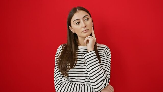Young beautiful hispanic woman wearing stripes t shirt standing thinking concentrated about doubt with finger on chin and looking up wondering over isolated red background