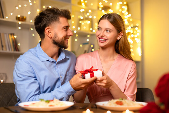 Man giving gift to happy woman, both smiling at dinner