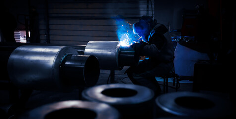 The welder works in the workshop with large-sized tube. Welding equipment and workwear. Sparks and...