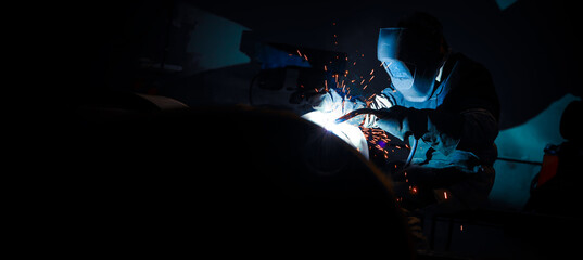 The welder is at work. Sparks and red-hot metal particles flying around. Welding equipment and workwear. - obrazy, fototapety, plakaty