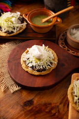 Fototapeta na wymiar Sopes. Mexican typical food prepared with flattened fried corn dough covered with refried beans, green or red sauce, lettuce, cheese, onion and sour cream. Mexican antojitos.