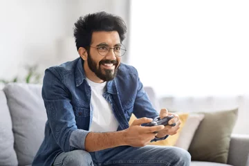 Fotobehang Cheerful young Indian man enjoying playing video games at home © Prostock-studio