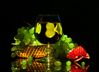 Wine glass with white wine and grapes, pomegranate on black background - 707535461