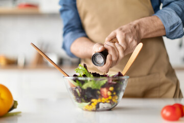 Focused elderly chef preparing nutritious vegetable salad, adding spices for flavor