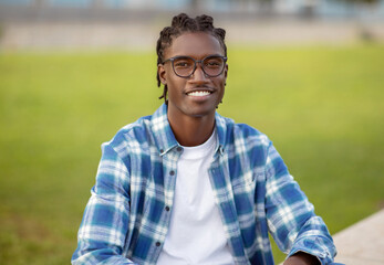 Naklejka na ściany i meble Cheerful young African American guy with stylish eyeglasses sitting outdoors