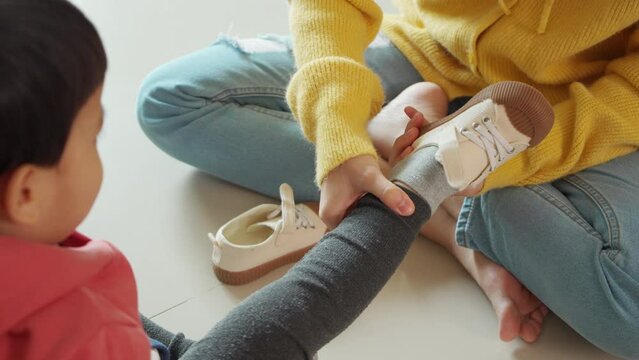 Asian mother helping her little son put on his shoes at home. First day of school.