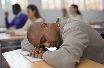 Portrait of tired hispanic man sleeping during lecture at adult education class..