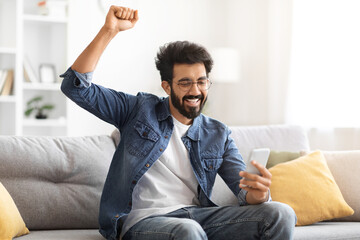 Great News. Overjoyed Indian Man Looking At Smartphone Screen And Celebrating Success
