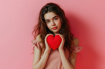 a beautiful girl holds up a red heart on pink background