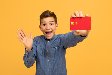 Happy surprised teen boy showing red credit card at camera - obrazy, fototapety, plakaty