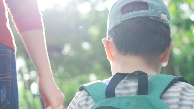 Asian Child boy and mother holding hands and walk in public park. Mom and son going to a preschool. Back to school.