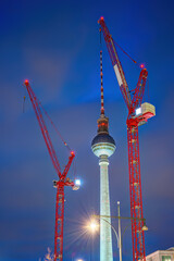 The famous Television Tower of Berlin at dusk with two red construction cranes - 707588886