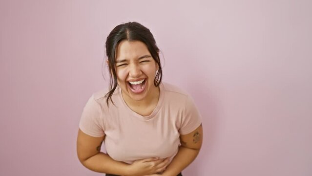 Upbeat young hispanic woman in t-shirt laughing out hard at a funny joke, smiling wide, standing over pink isolated backdrop. her joyful face filled with laughter radiates positive vibes.