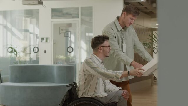 Businessman in wheelchair and his colleague searching for data on interactive digital screen and having discussion in modern coworking space