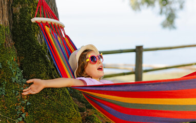 A child swings in a bright and vivid colors hammock outdoors. The child enjoys the clean fresh summer air in nature.