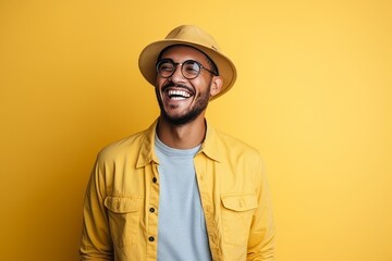 Portrait of a smiling hipster man in hat and glasses over yellow background
