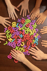Kids hands with colorful plastic numbers on brown table. Top view