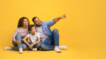 Check This. Happy black family sitting together and pointing at copy space