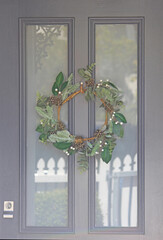 Christmas wreath hanging on a grey front door with glass panels